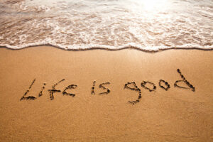 Words on beach that say "life is good" illustrating that happiness is a mindset