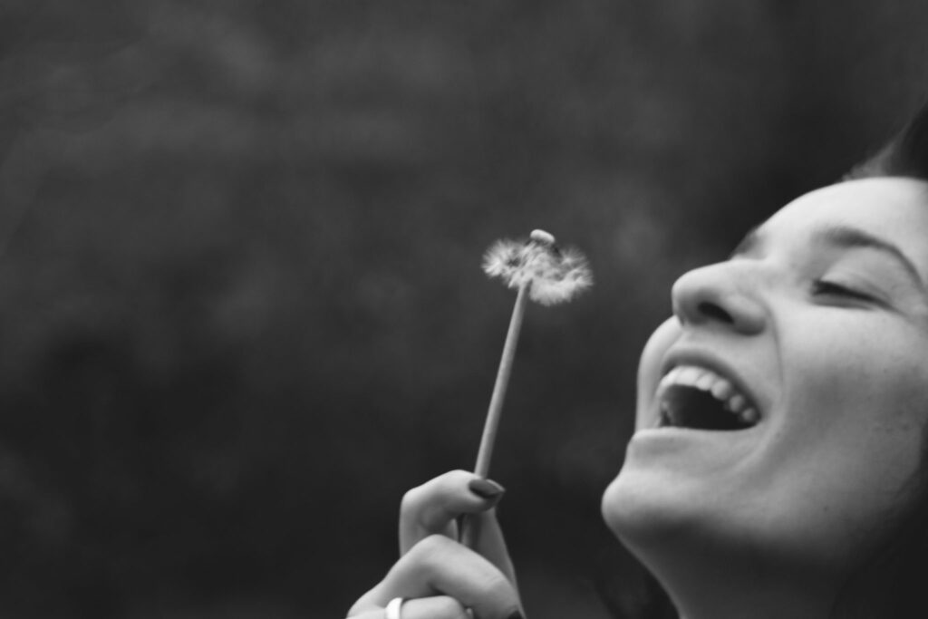 happy, optimistic woman blowing dandelion