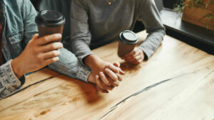 Couple holding hands, showing unity and love as they sip coffee.