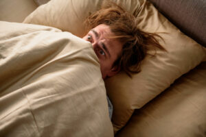 scared male lying in bed with covers pulled up to face